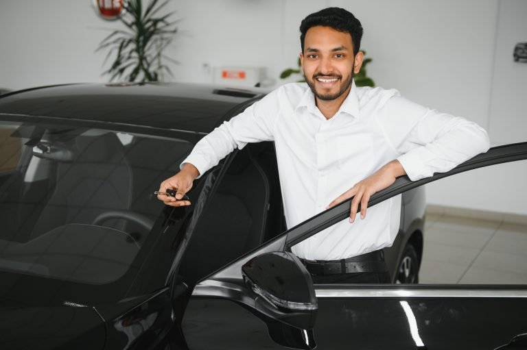 Smiling, friendly indian car seller standing in car salon.